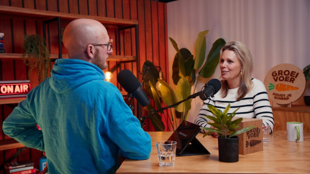 Twee personen zijn in gesprek tijdens een opname van de Groeivoer-podcast in een sfeervolle studio.