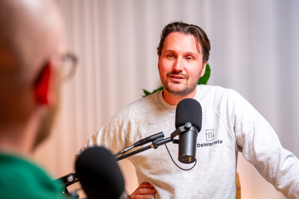 Man in een grijze trui met het logo van DeWarmte spreekt in een microfoon tijdens de Groeivoer Podcast.