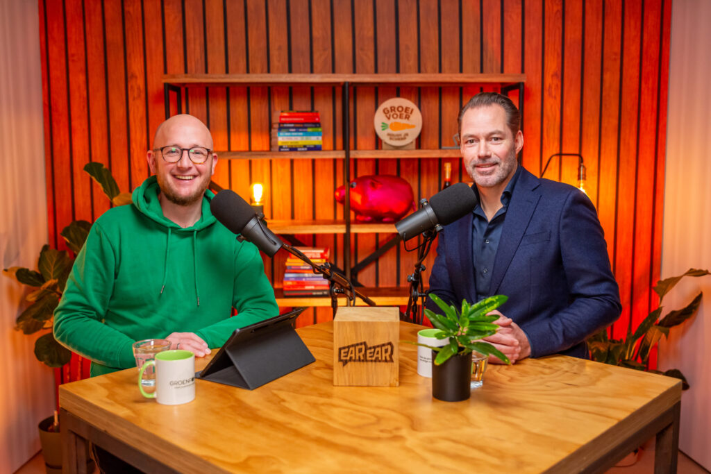 Twee mannen zitten lachend achter microfoons in een kleurrijke studio tijdens de opname van de Groeivoer-podcast.