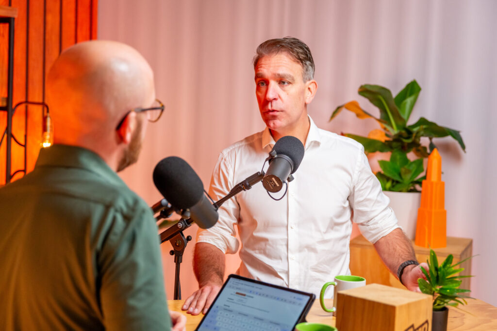 Twee mannen in gesprek tijdens een opname van de Groeivoer Podcast, met microfoons en een laptop op tafel.