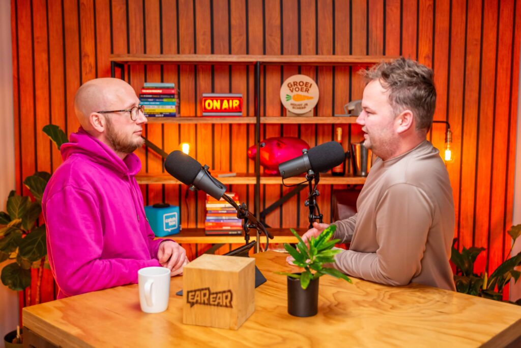 Twee mannen in gesprek tijdens de opname van de Groeivoer-podcast, zittend aan een tafel met microfoons in een kleurrijke studio.