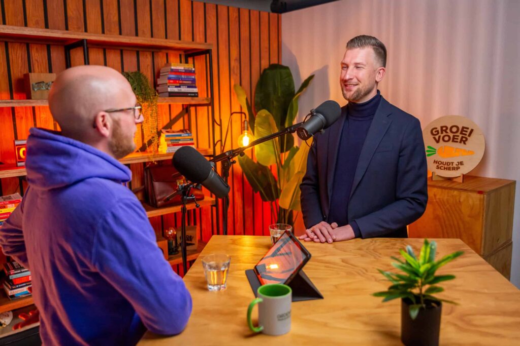 Twee mannen voeren een gesprek in een kleurrijke podcaststudio met "Groeivoer" branding op de achtergrond.