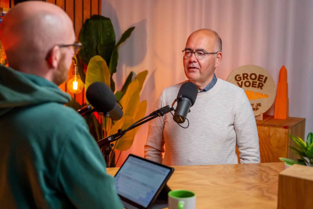 Twee mannen in gesprek tijdens een opname van de Groeivoer-podcast, zittend aan een houten tafel met microfoons en een laptop.