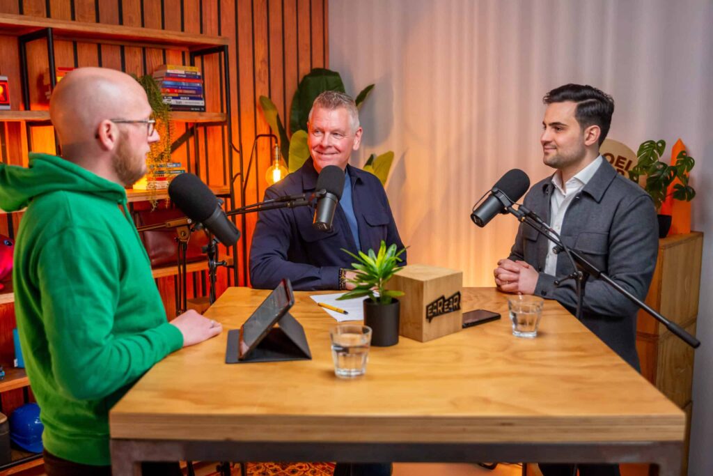 Drie mannen zitten aan een houten tafel in een gezellige studio-opstelling tijdens een opname van de Groeivoer-podcast.