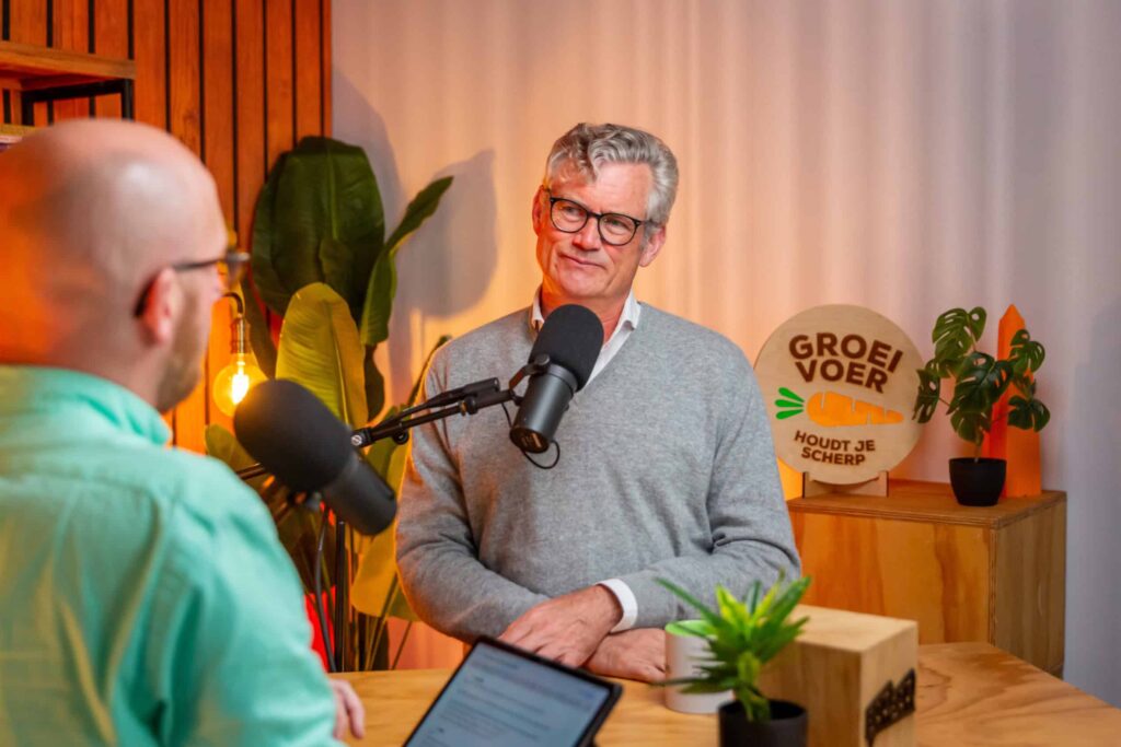 Twee mannen in gesprek tijdens een opname van de Groeivoer Podcast, met microfoons en het podcastlogo op de achtergrond.