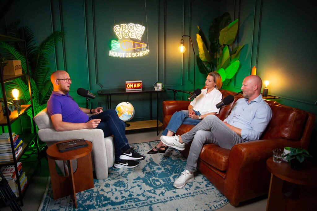 Drie mensen in gesprek tijdens een opname van de Groeivoer-podcast in een sfeervolle studio met neonverlichting en microfoons.