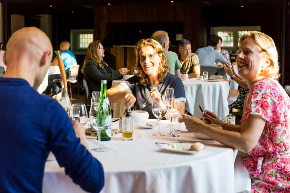 Groep ondernemers in gesprek tijdens een mastermind-bijeenkomst aan een ronde eettafel.