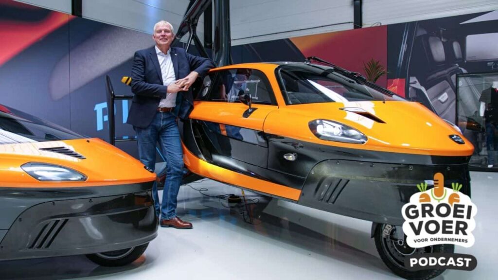 Man poseert naast een futuristisch ogende oranje-zwarte auto in een showroom, met het logo van de Groei Voor Ondernemers-podcast rechtsonder in beeld.