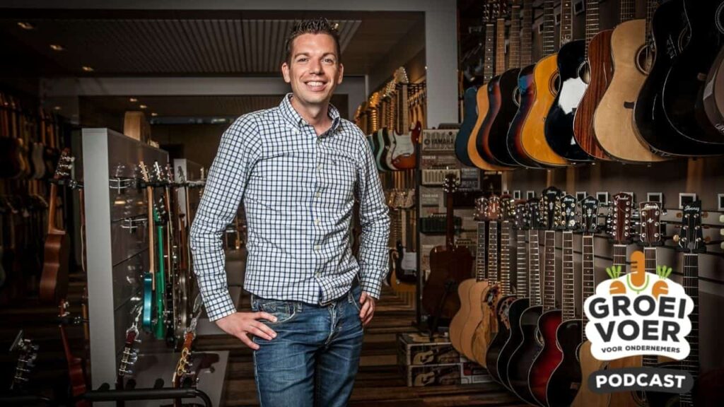 Jochanan Bax poseert glimlachend in een gitaarwinkel voor de Groeivoer Podcast voor ondernemers.