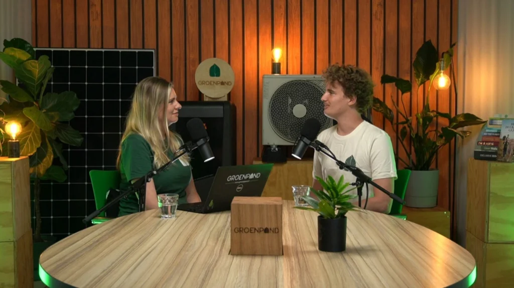 Twee mensen voeren een gesprek in de Groenpand-podcaststudio met microfoons en planten op de achtergrond.