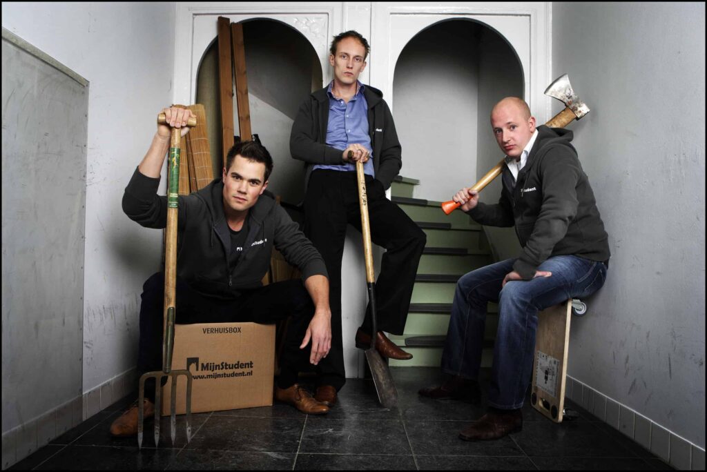 Drie voormalig compagnons van MijnStudent poseren met gereedschap in een trappenhuis voor een groepsfoto.