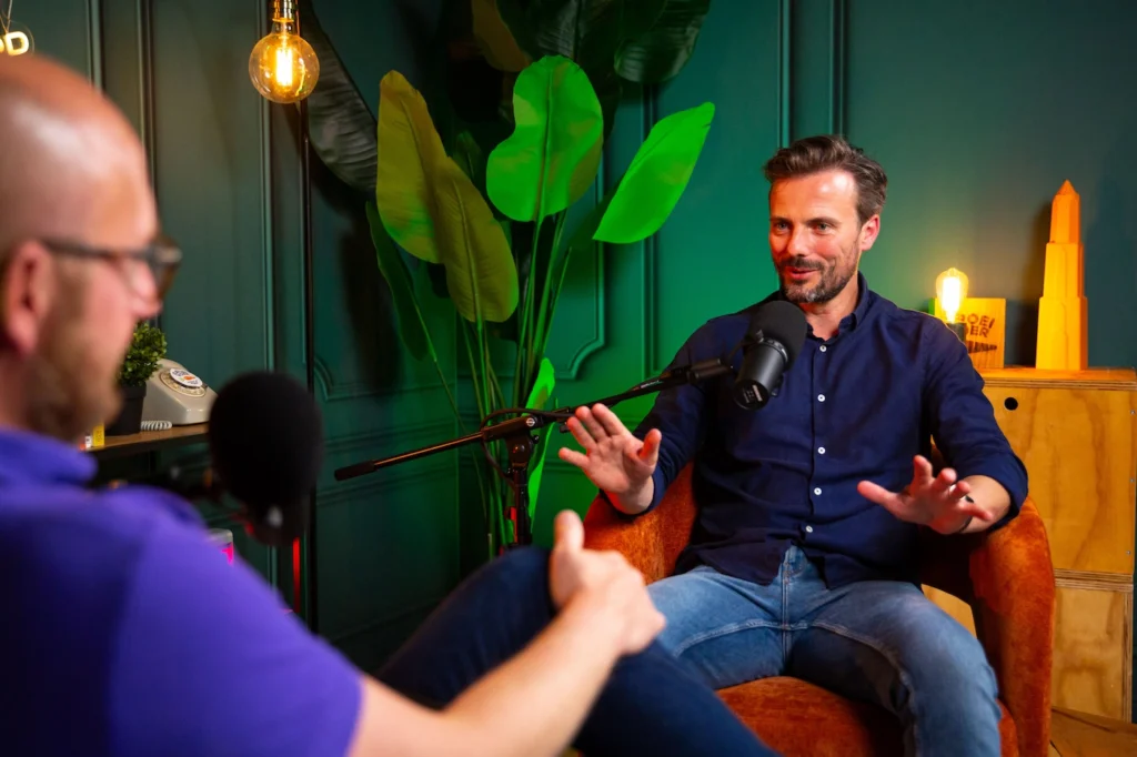 Gerhard voert een gesprek met een gast tijdens een podcastopname in een kleurrijke studio.