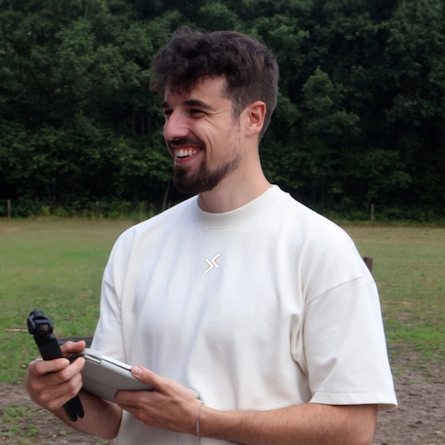 Man van Team Jay lacht terwijl hij buiten een camera en tablet vasthoudt.