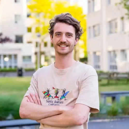 Man genaamd Lars poseert lachend met gekruiste armen buiten voor een gebouw.