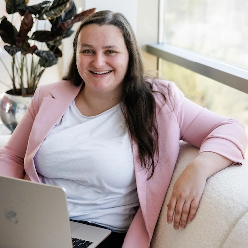 Vrouw van Team Maud zit lachend met een laptop op schoot in een lichte, moderne kantoorruimte.