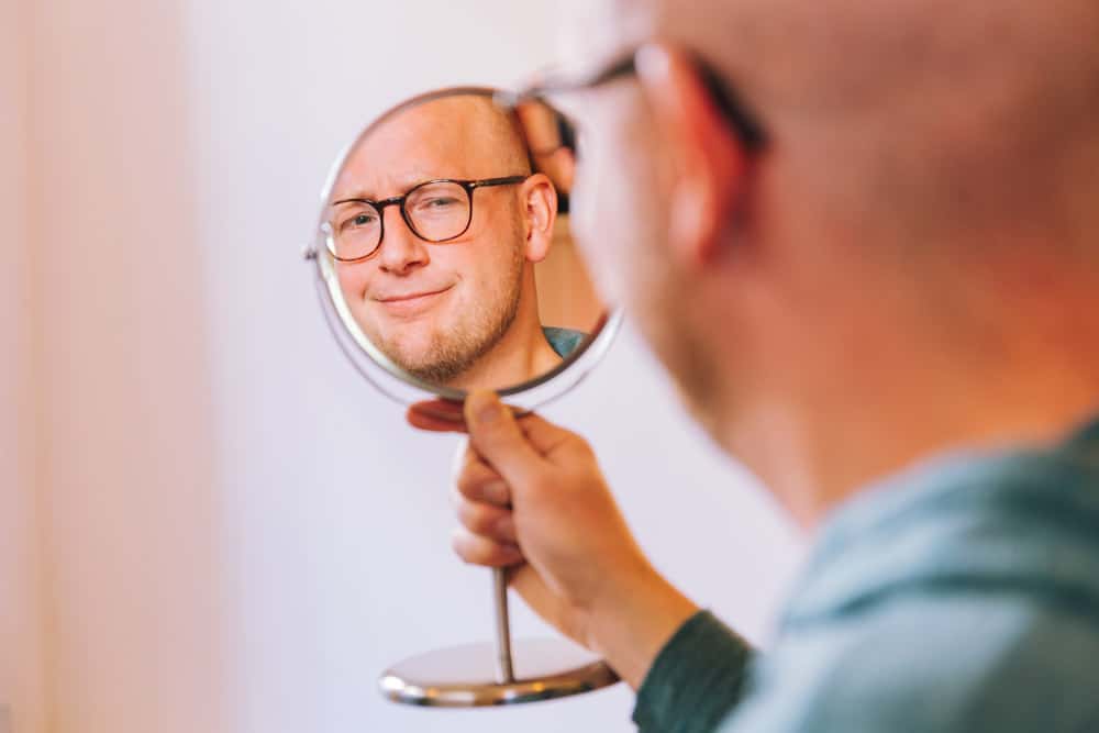 Man houdt een spiegel vast en kijkt met een bedachtzame blik naar zijn eigen reflectie.