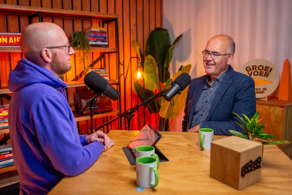 Twee mannen zitten tegenover elkaar in een kleurrijke podcaststudio en voeren een gesprek voor de Groeivoer Podcast.