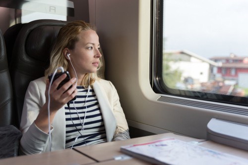 Vrouw luistert naar muziek en kijkt uit het raam tijdens een treinreis.
